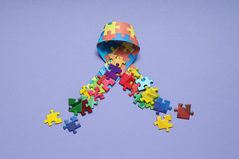ribbon-with-multicolored-puzzle-pieces-light-background-world-autism-day-concept-scaled